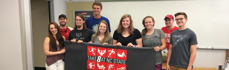 Students holding a Take 8 at State banner