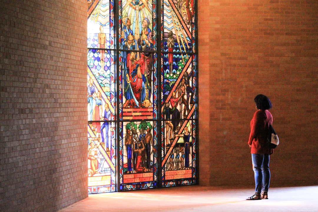 Student stands in front of a stained glass window