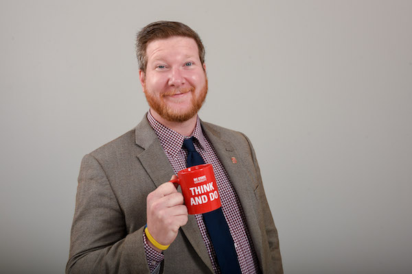 Brian Mathis holds a coffee cup and smiles at the camera.