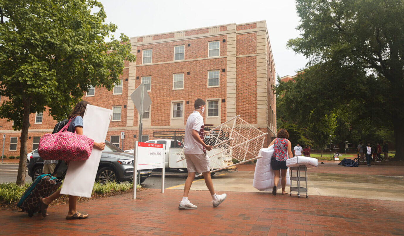 A new student and family carry their belongings towards a residence hall