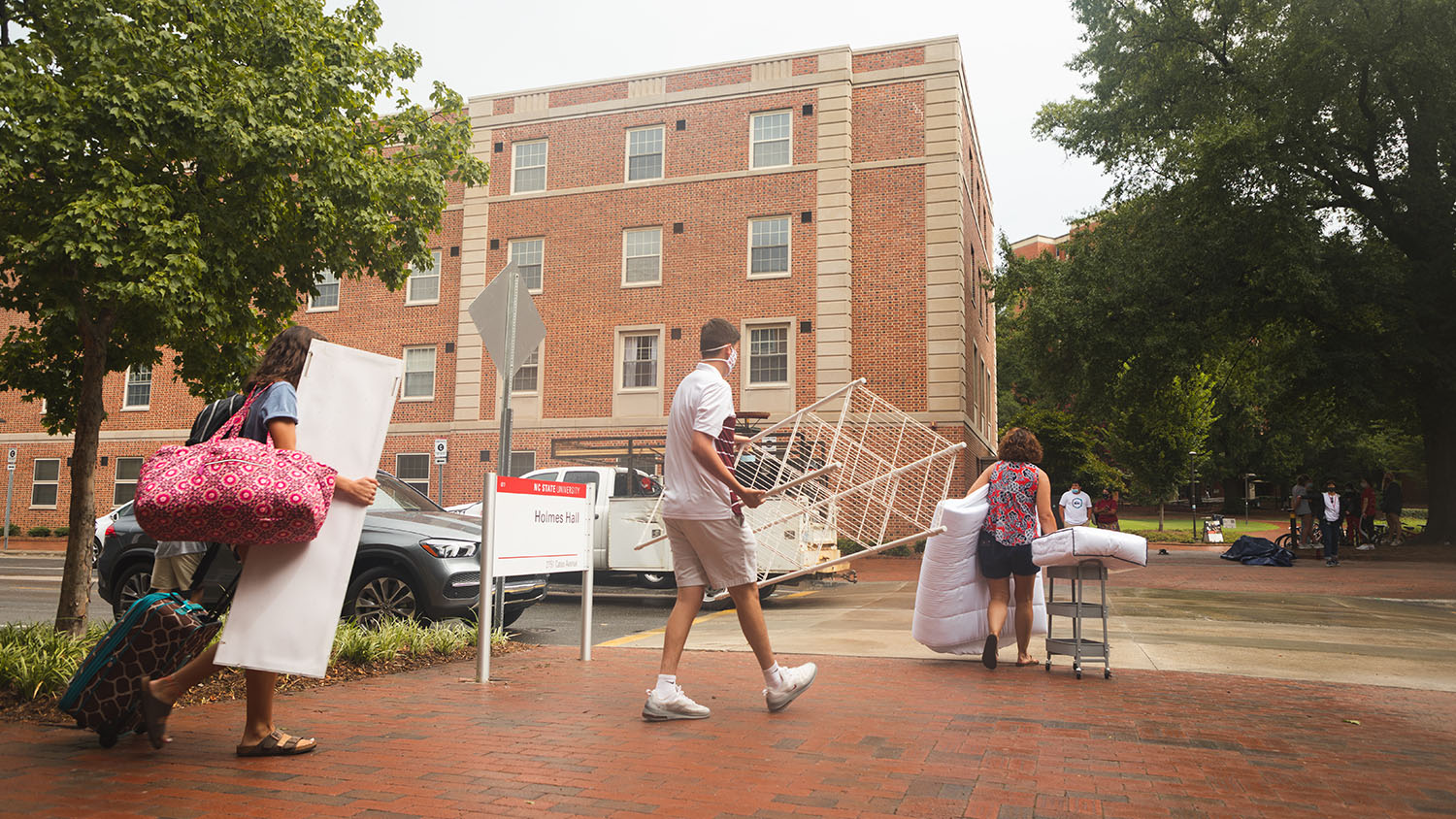 A new student carries luggage towards his residence hall
