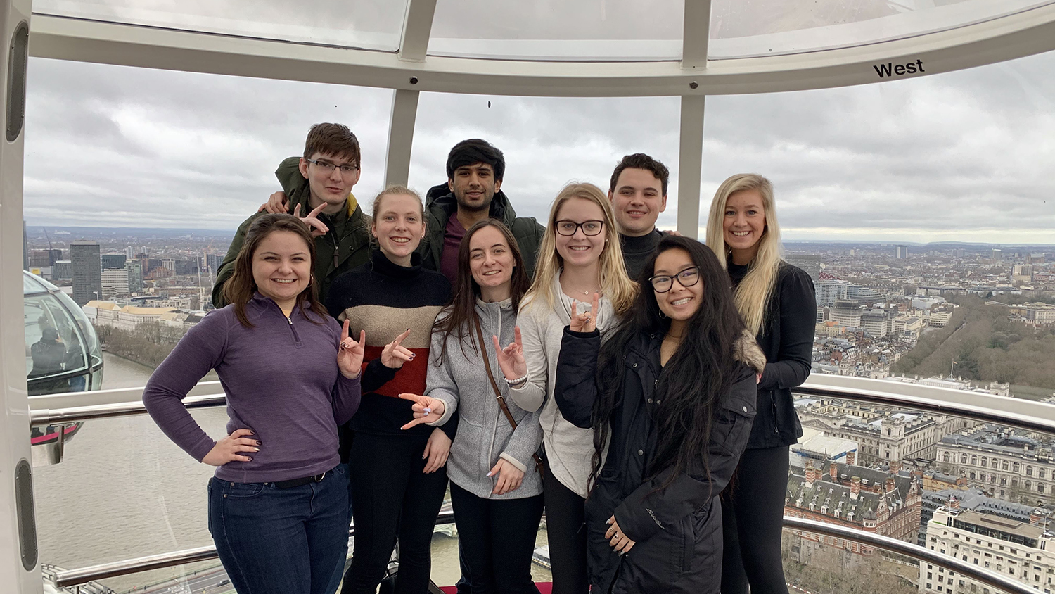Students pose high above the city of London in a glass observation pod.