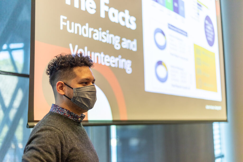A masked student stands in front of a screen about volunteering