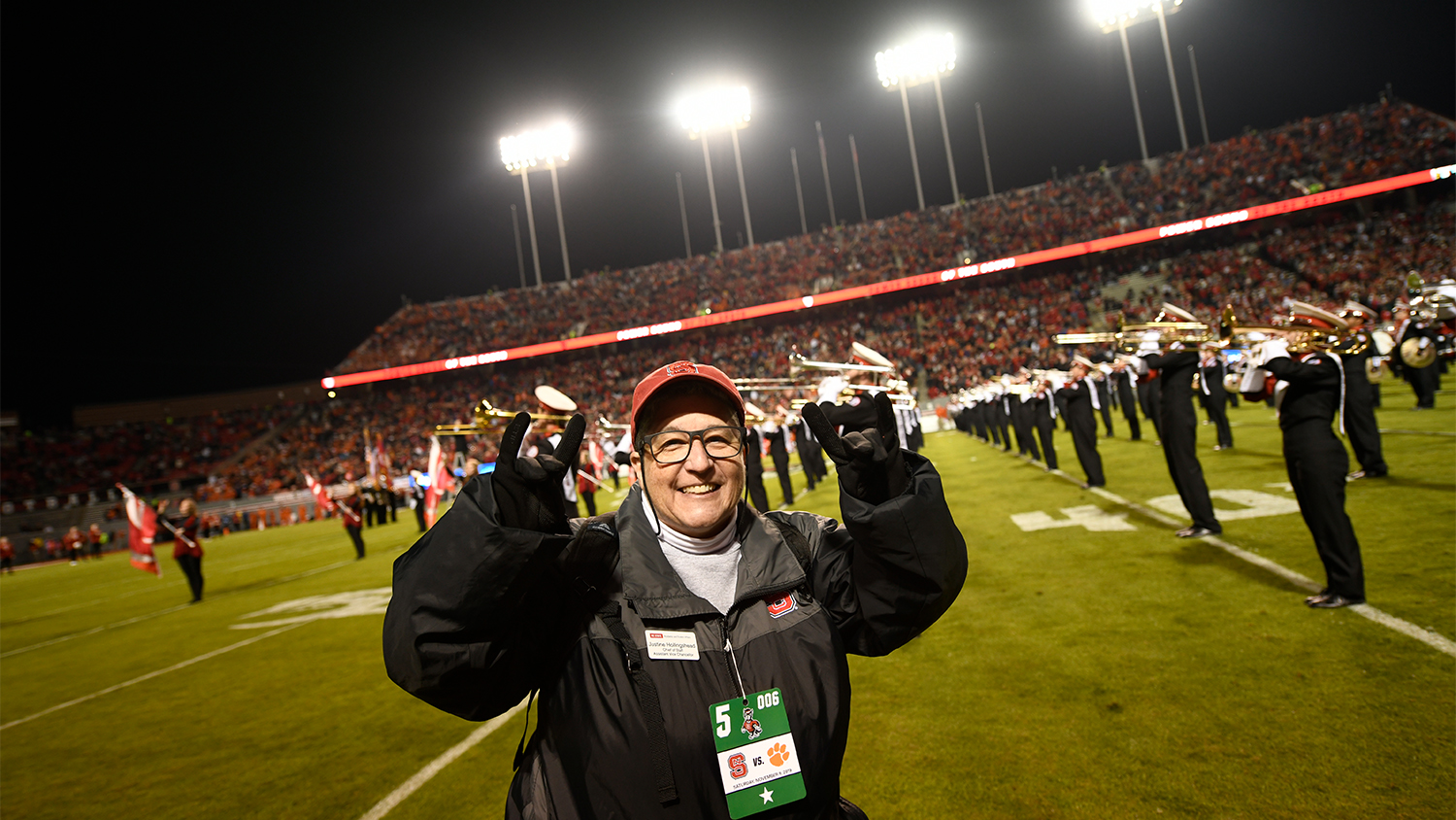 Justine Hollingshead making a wolfie sign on the field at an NC State football game