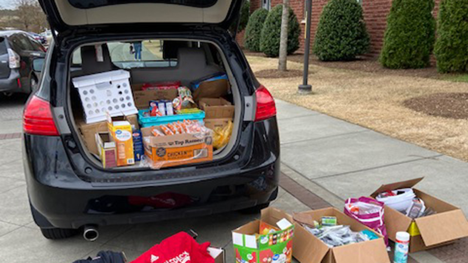 Back of a car with boxes of donated supplies in the truck and on the ground.