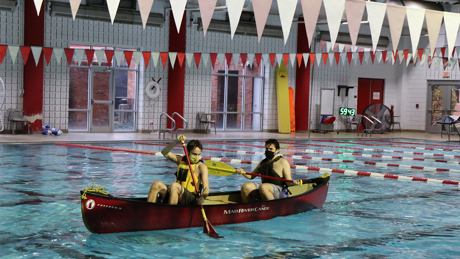 Two students use paddles in a canoe in an indoor swimming pool