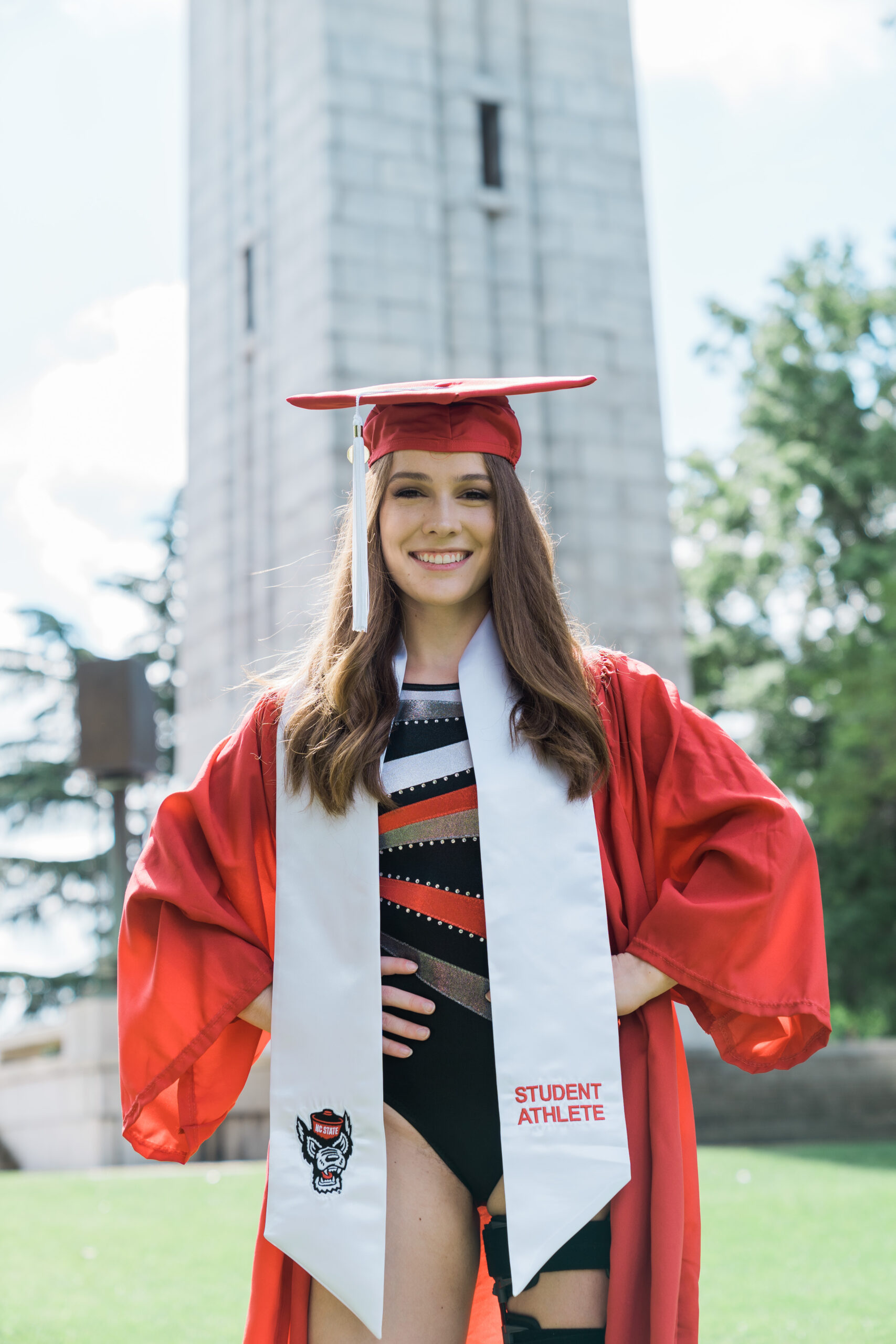 A female student-athlete in cap and gown, posing in front of the Bell Tower