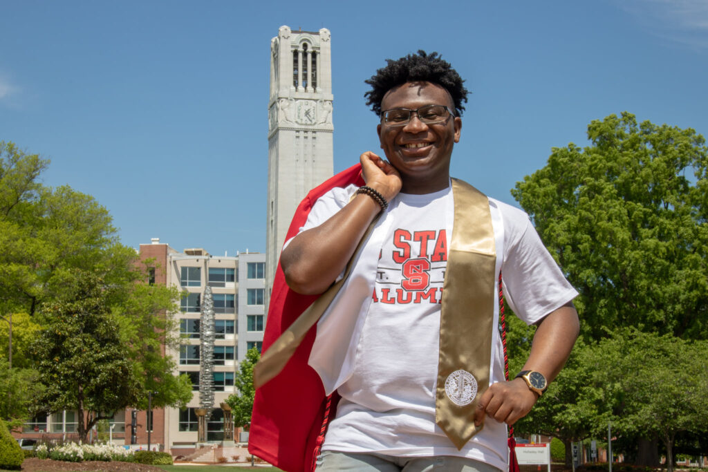 Tirrezz Hudson with a red graduation robe slung over his shoulder, bell tower in the background