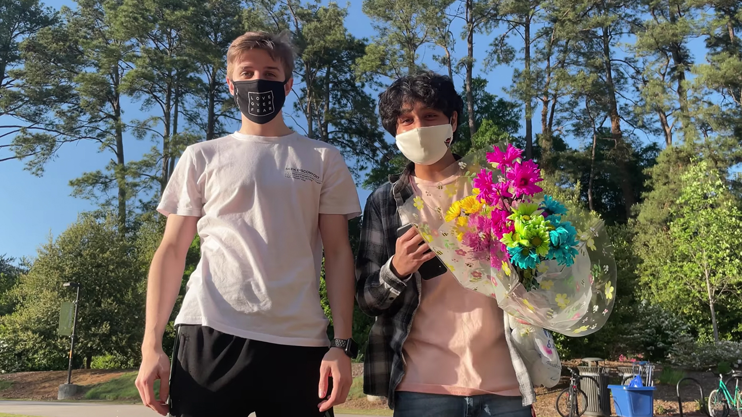 Sean Deardorff and Tejas Kakade wearing masks, holding flowers in an outdoor setting
