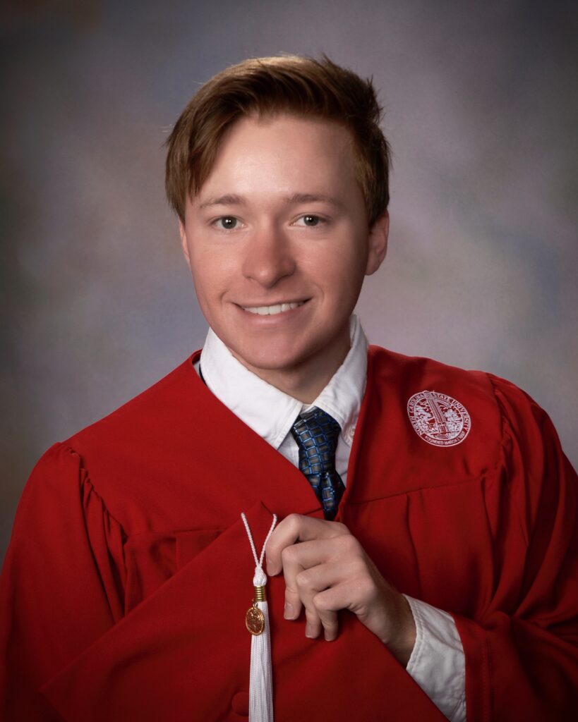 Noah Jabusch in red graduation robe, holding his cap in front of him