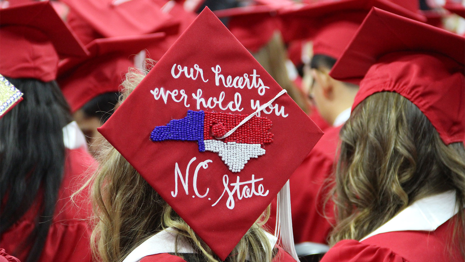 The top of a graduate's hat that reads "Our hearts ever hold you, NC State"