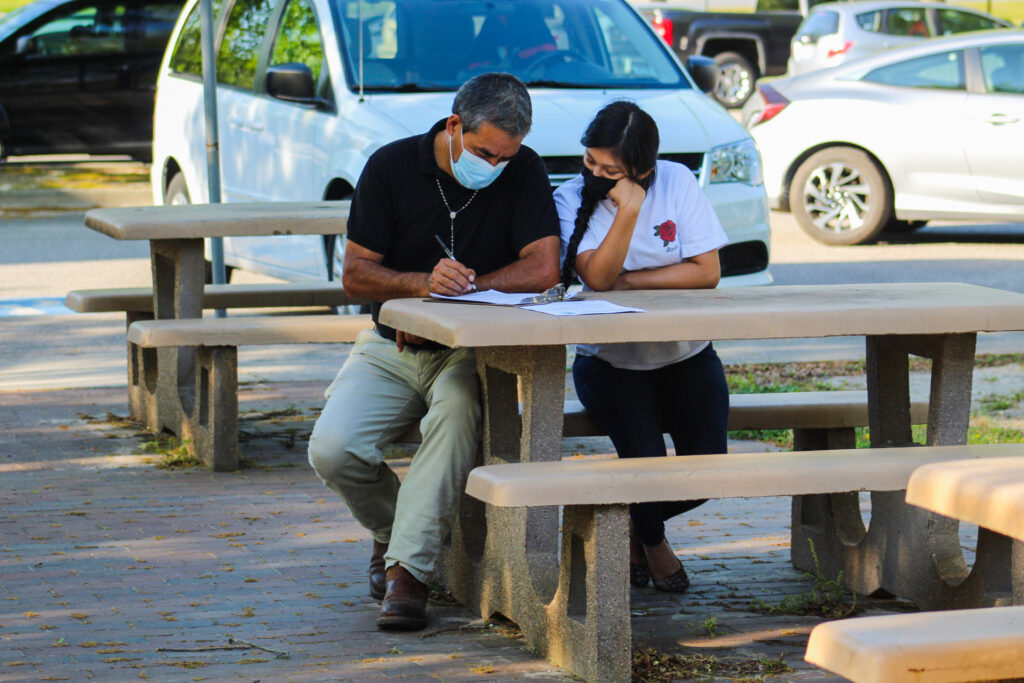 A student and parent, seated at a picnic table, fill out college forms together