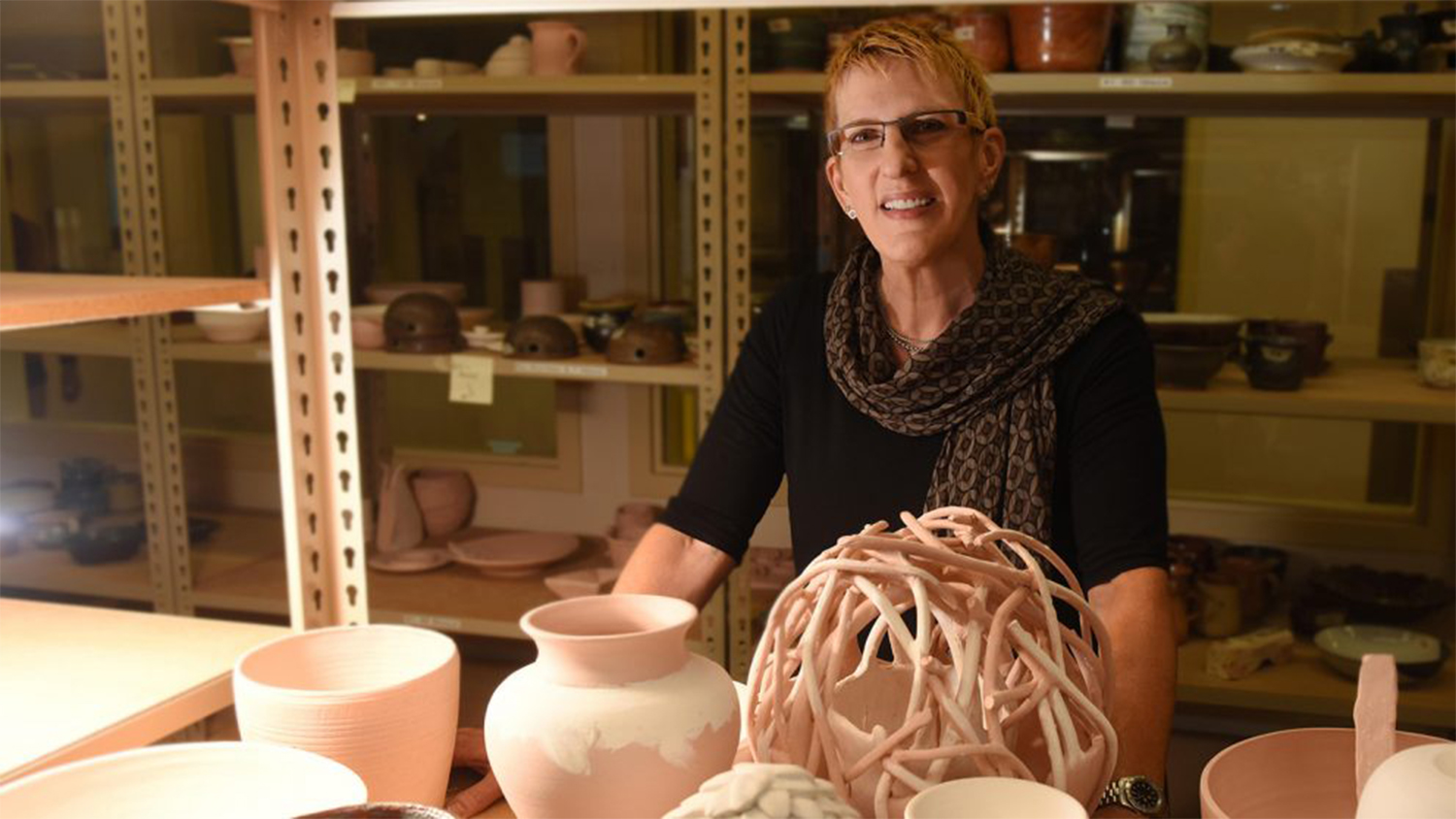 Carol Fountain Nix sitting at a desk with pottery displayed in front of her