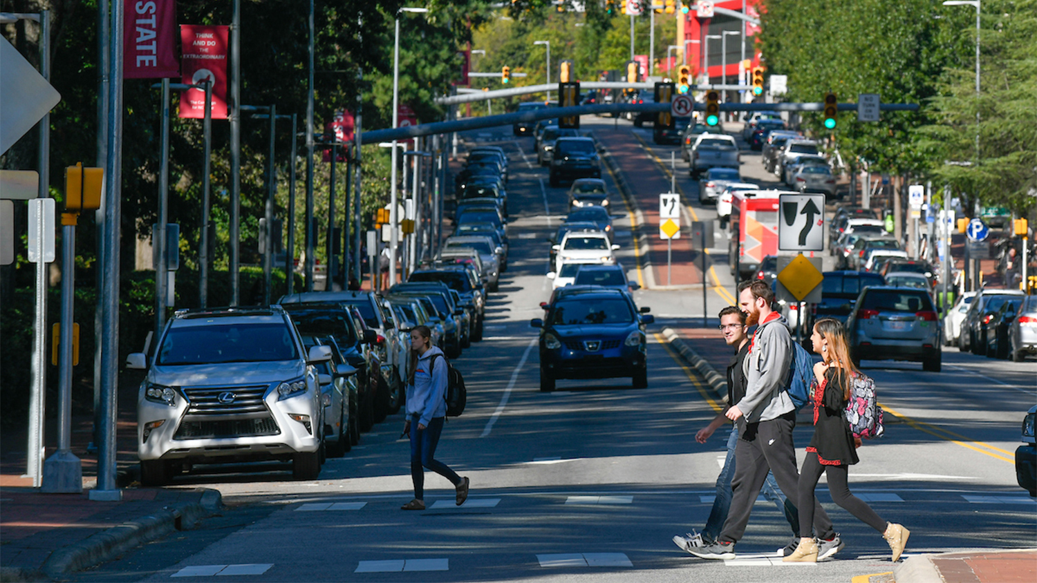 Students use a cross walk to cross Hillsborough Street, with several cars in both directions in the background