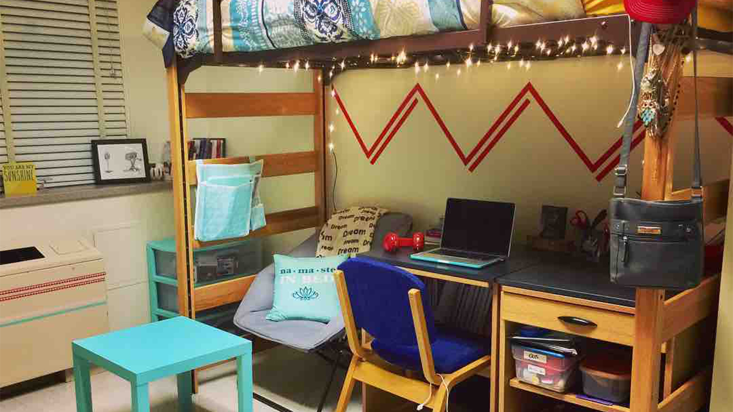 A residence hall room with lofted bed with a desk and fold out chair underneath
