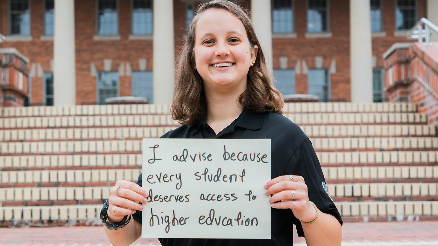 Kiera Lindner holds a sign that reads "I advise because every student deserves access to higher education"