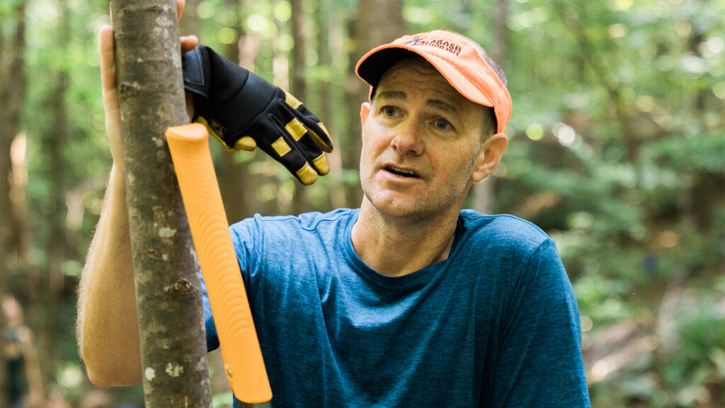 Tommy Holden leans against a small tree in Lake Raleigh Woods while working on a bike trail reroute project.