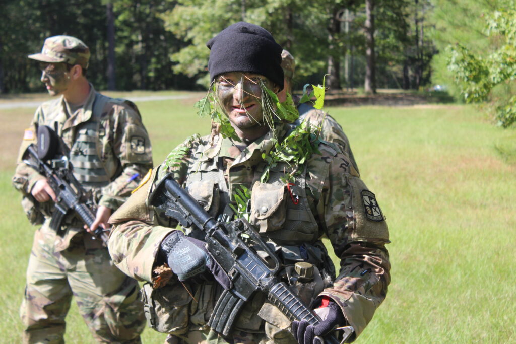 Cadets in full camouflage hold M4 rifles as they walk through a field