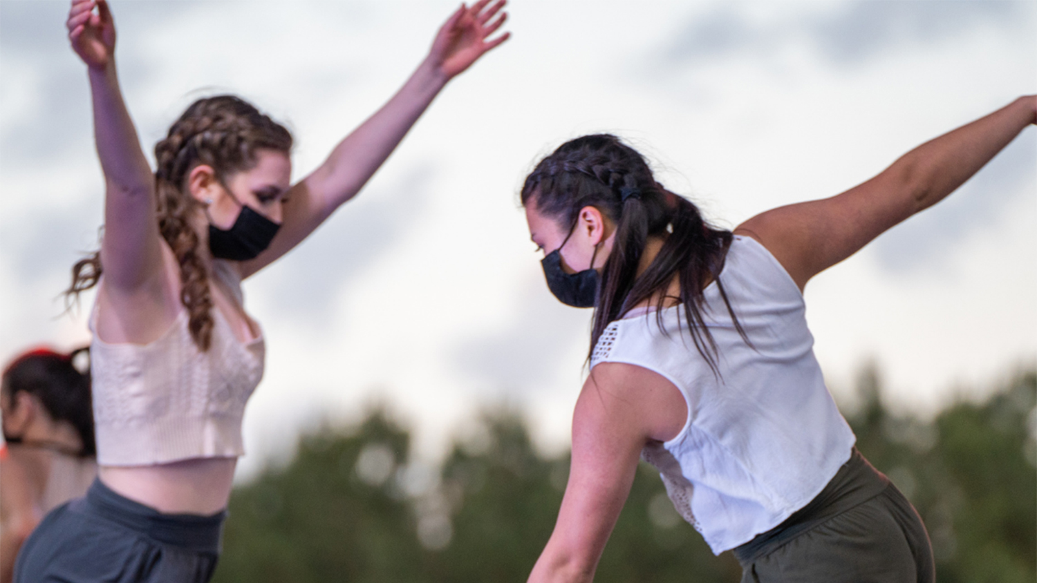 Two masked students perform a dance routine outdoors