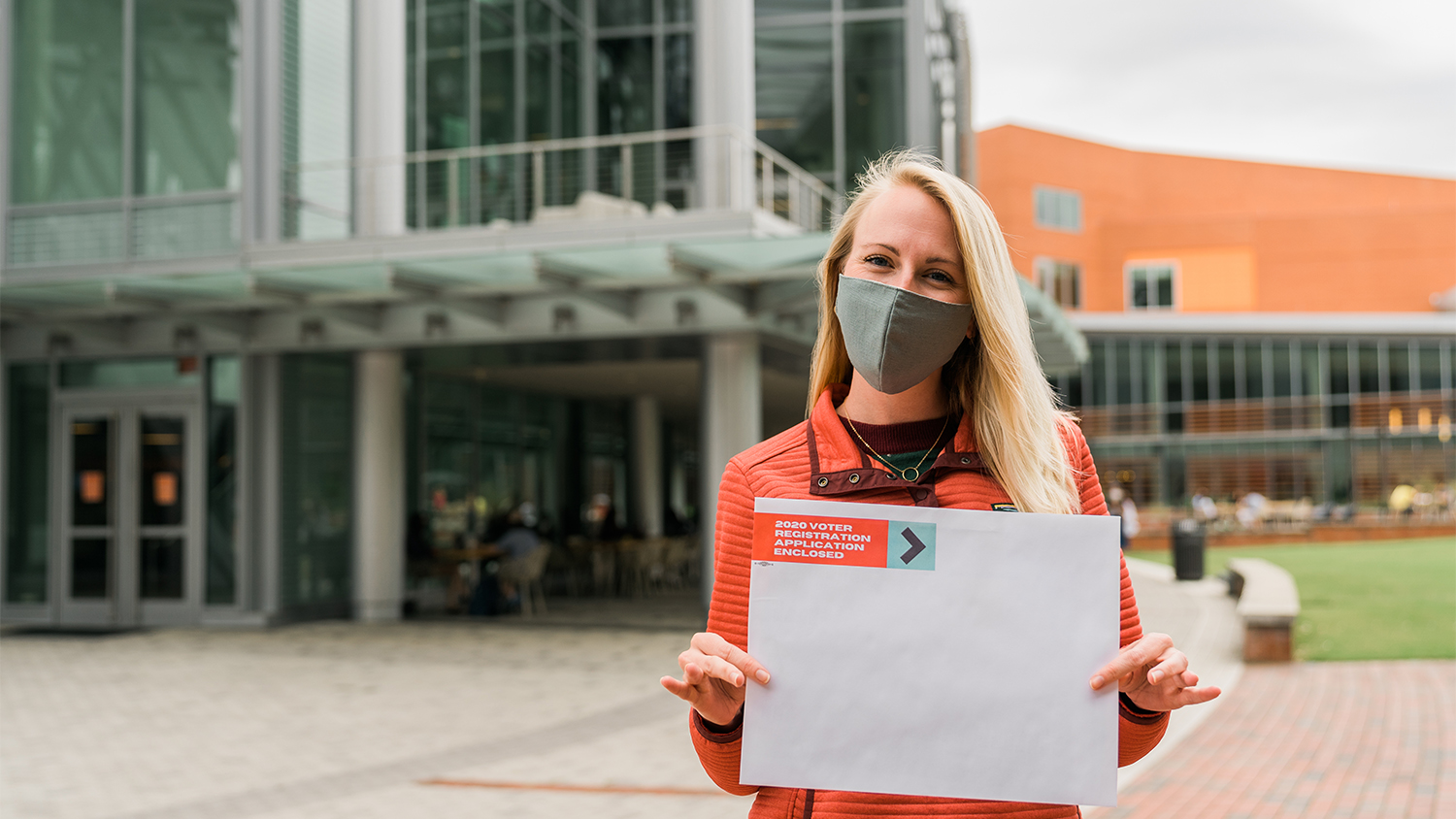 A student in front of Talley Student Union holds an envelope labeled "2020 voter registration application enclosed"