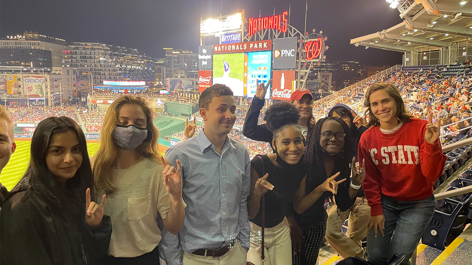 A group of NC State students in the stands at a Washington Nationals game, making wolfie signs