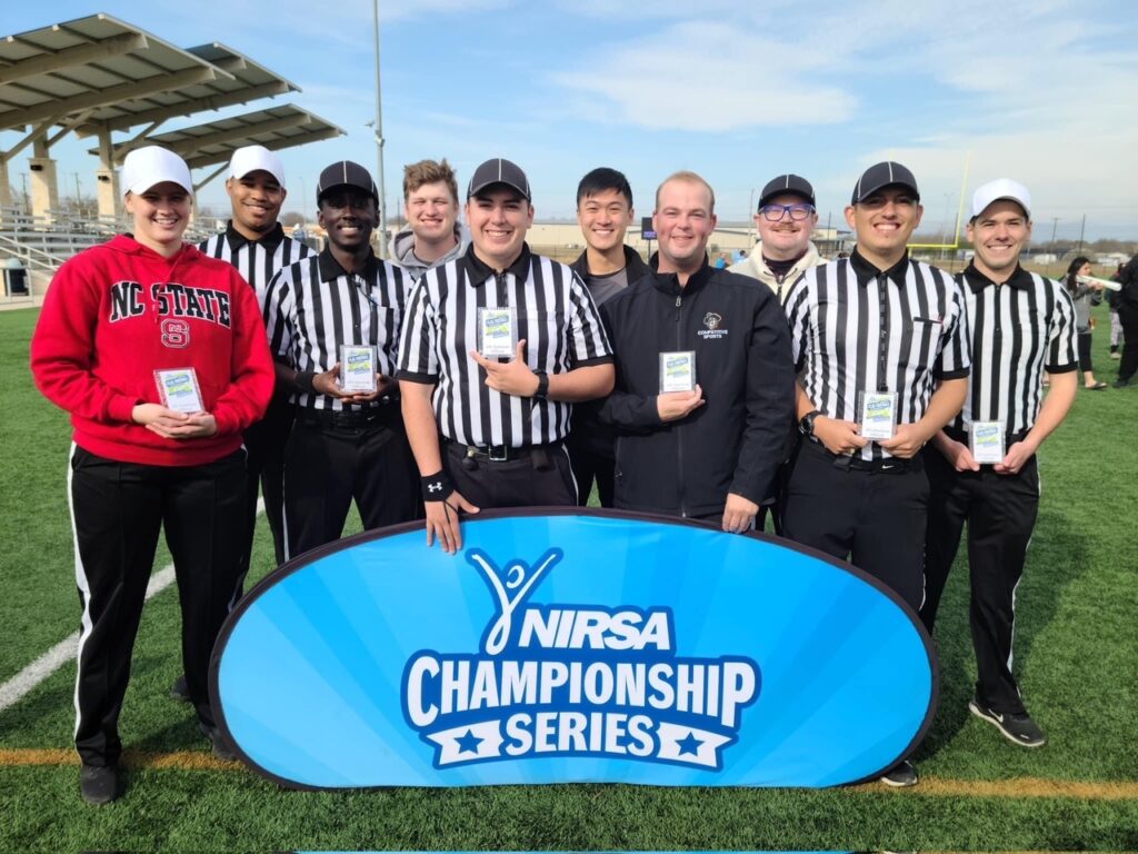Hannah Williams in an NC State sweatshirt and holding a small plaque, posing with other referees on a field