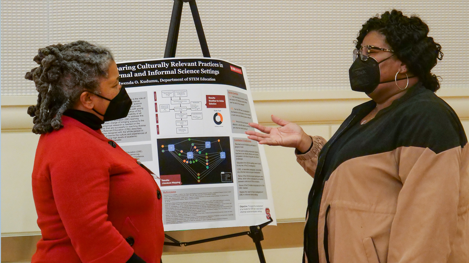 Two people speak in front of a poster presentation