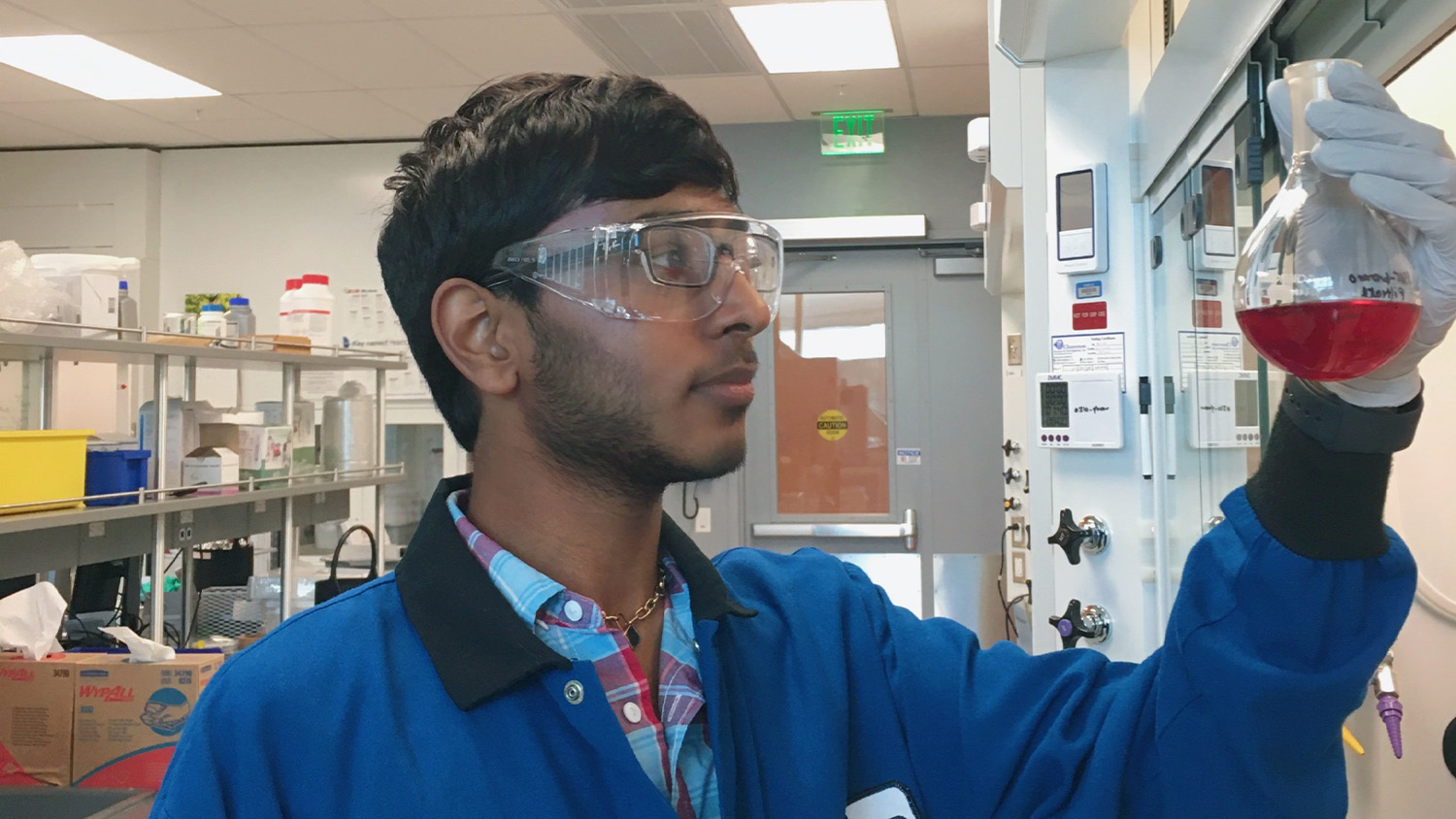 Kiran Soma holds up a beaker filled with red liquid inside a laboratory