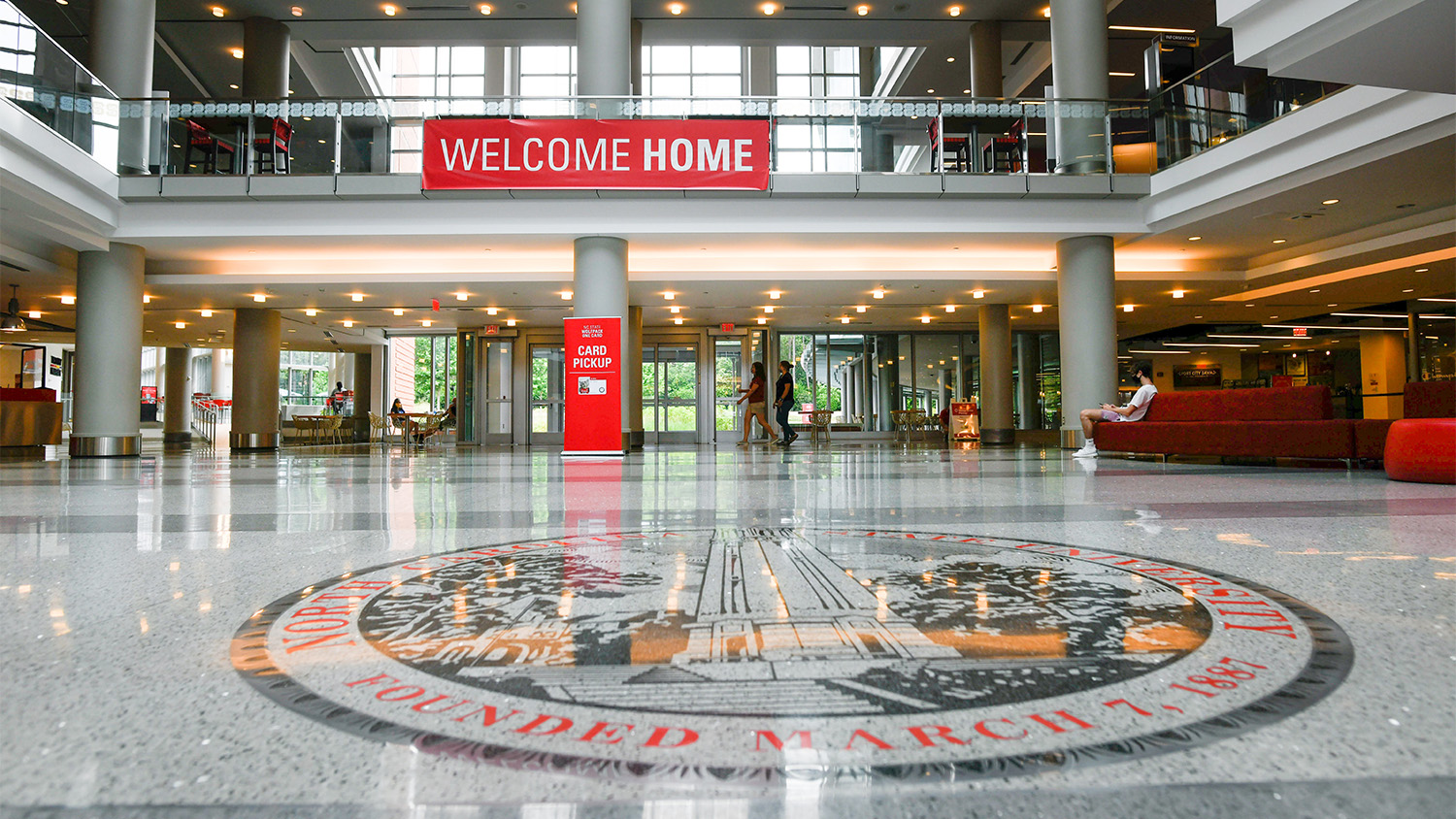 The NC State seal on the floor of Talley Student Union, with a large banner in the background that reads "Welcome Home."