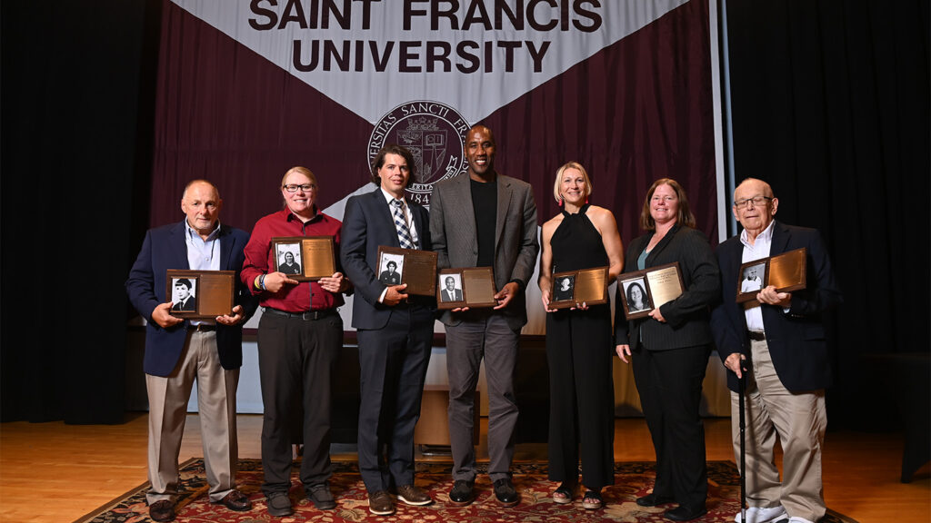 Megan Albidrez and other Saint Francis Athletics Hall of Fame inductees hold up their plaques on stage