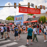 Large crowds walk down Hillsborough Street under a large red banner saying "Welcome to Packapalooza."