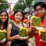 Three students hold up pineapples with straws in them