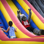 Mr. Wuf holds up wolfies while going down an inflatable slide