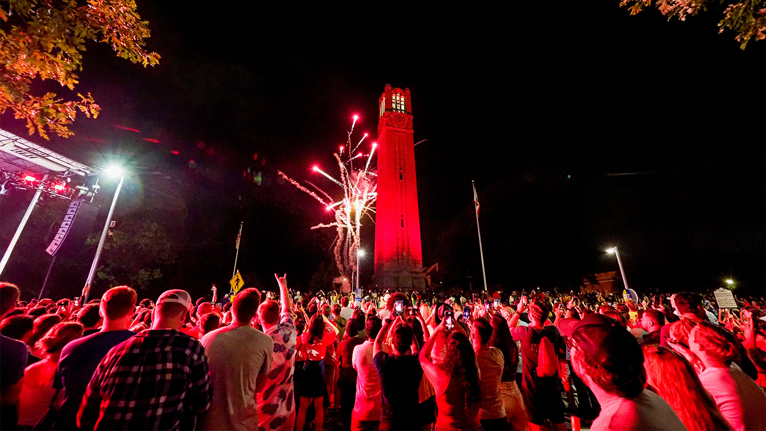 The Memorial Belltower at night, illuminated in red with lots of students at the bottom