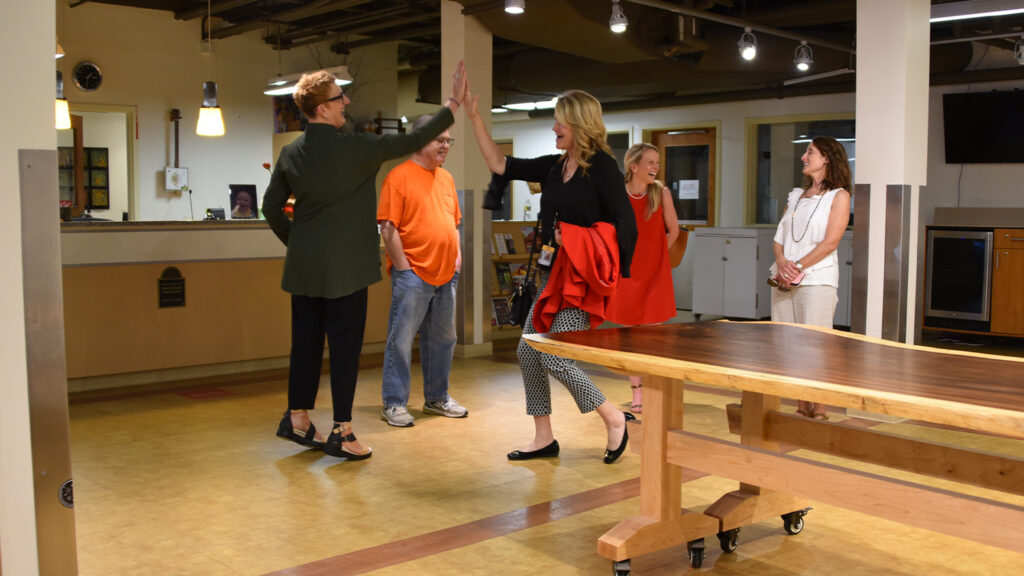 Two people celebrate with a high five next to the wooden table in the Crafts Center lobby