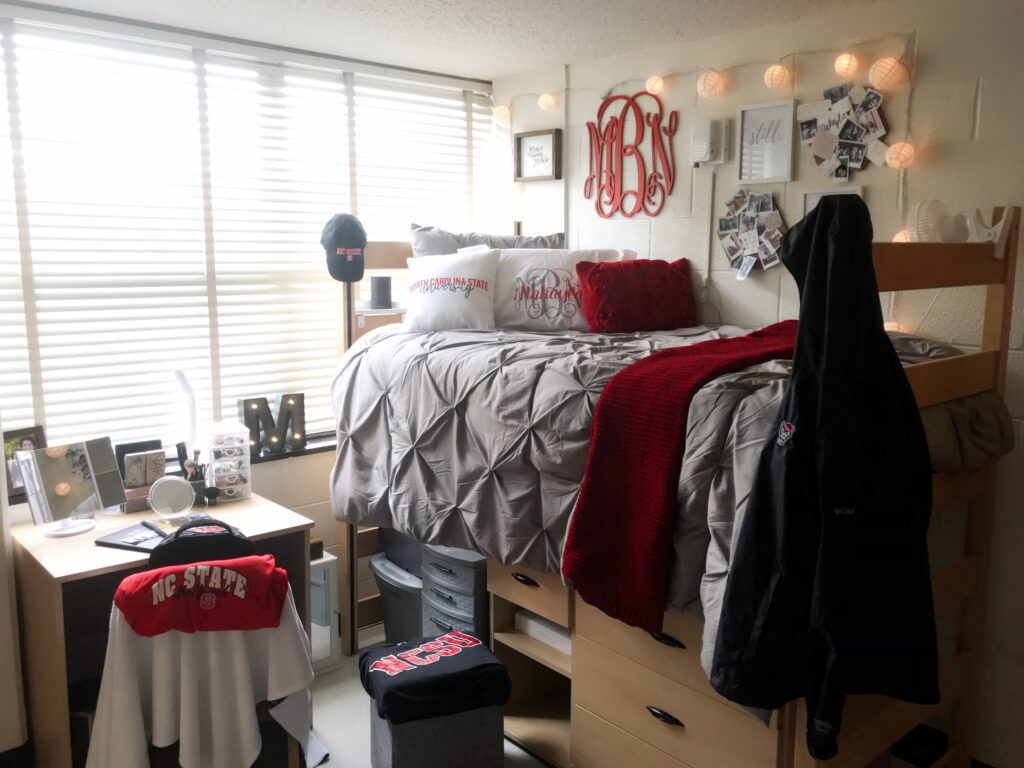 A residence hall room with a lofted bed and NC State red accents