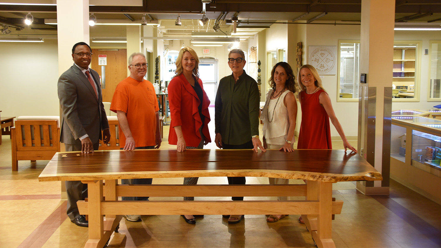 A group of people behind a hand-carved wooden table, positioned in the center of the Crafts Center lobby