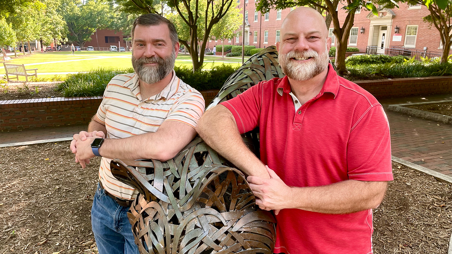 Heath Ramsey and Christopher Leazer pose by a wolf statue in Wolf Plaza