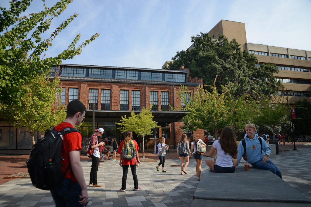 Students walk by a brick building with green trees nearby