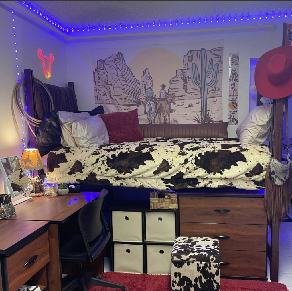 A resident's room, showing a lofted bed with a cow-patterned blanket and a red cowboy hat hanging on the bed post