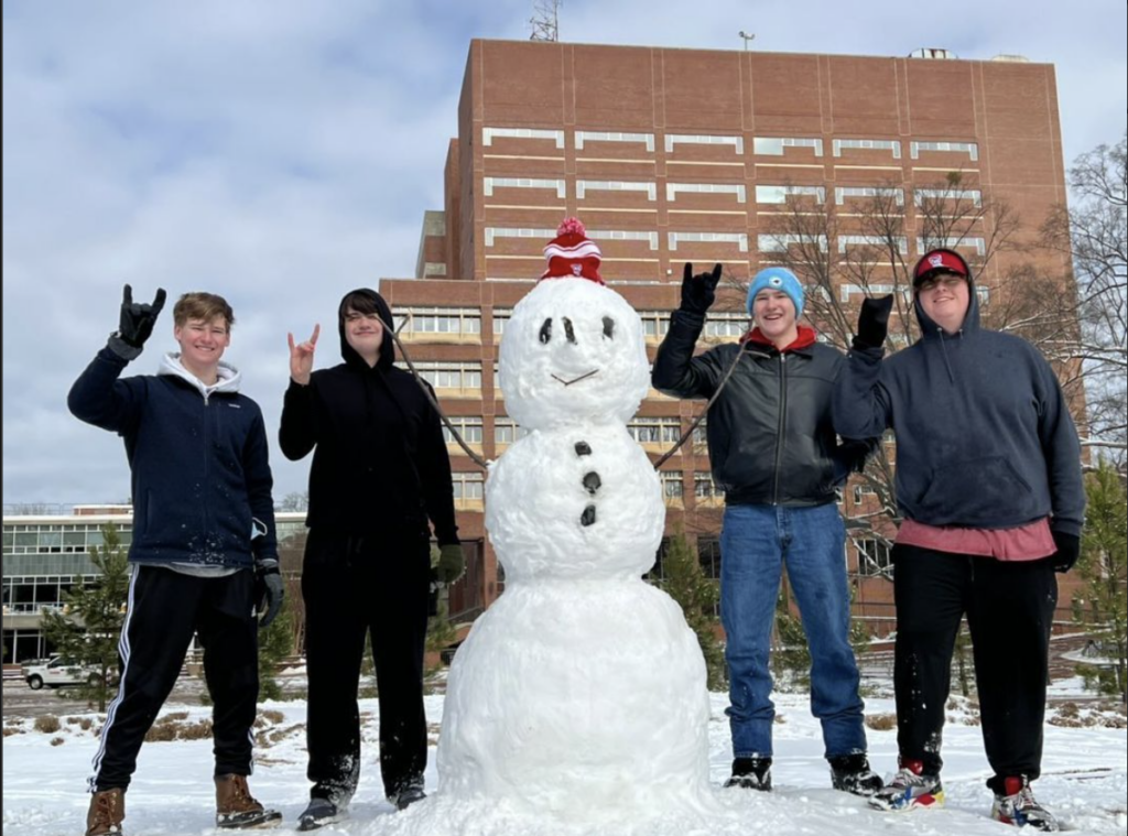 Students pose with a snow man in front of Hill Library