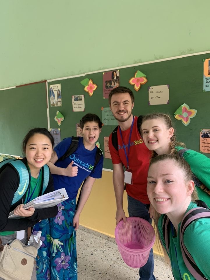 Minor and four other students leaning in for a selfie in a classroom with green walls and a green bulletin board