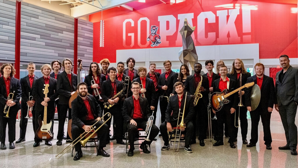 The NC State Jazz Orchestra with their instruments in front of a sign that says "Go Pack"