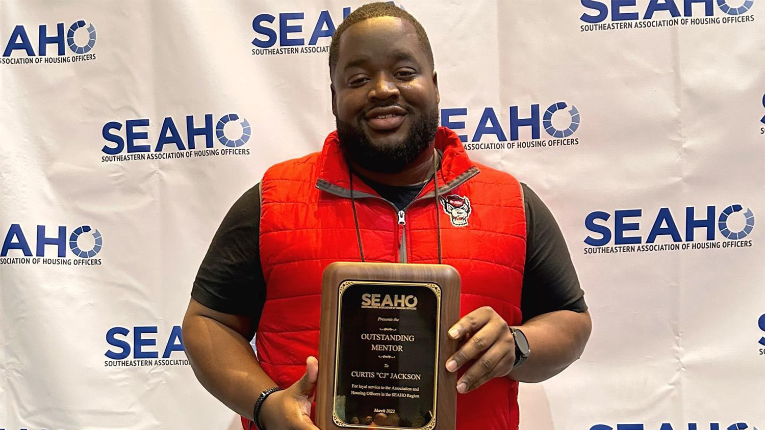 Curtis "CJ" Jackson holding a plaque in front of a white backdrop with the SEAHO logo on it
