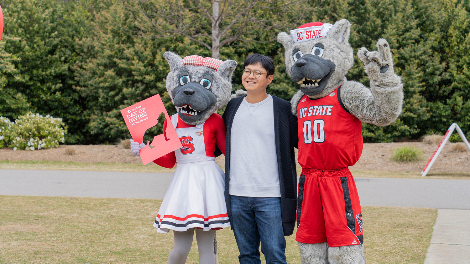 Mr and Ms. Wuf pose with a student on Stafford Commons while holding Day of Giving signs