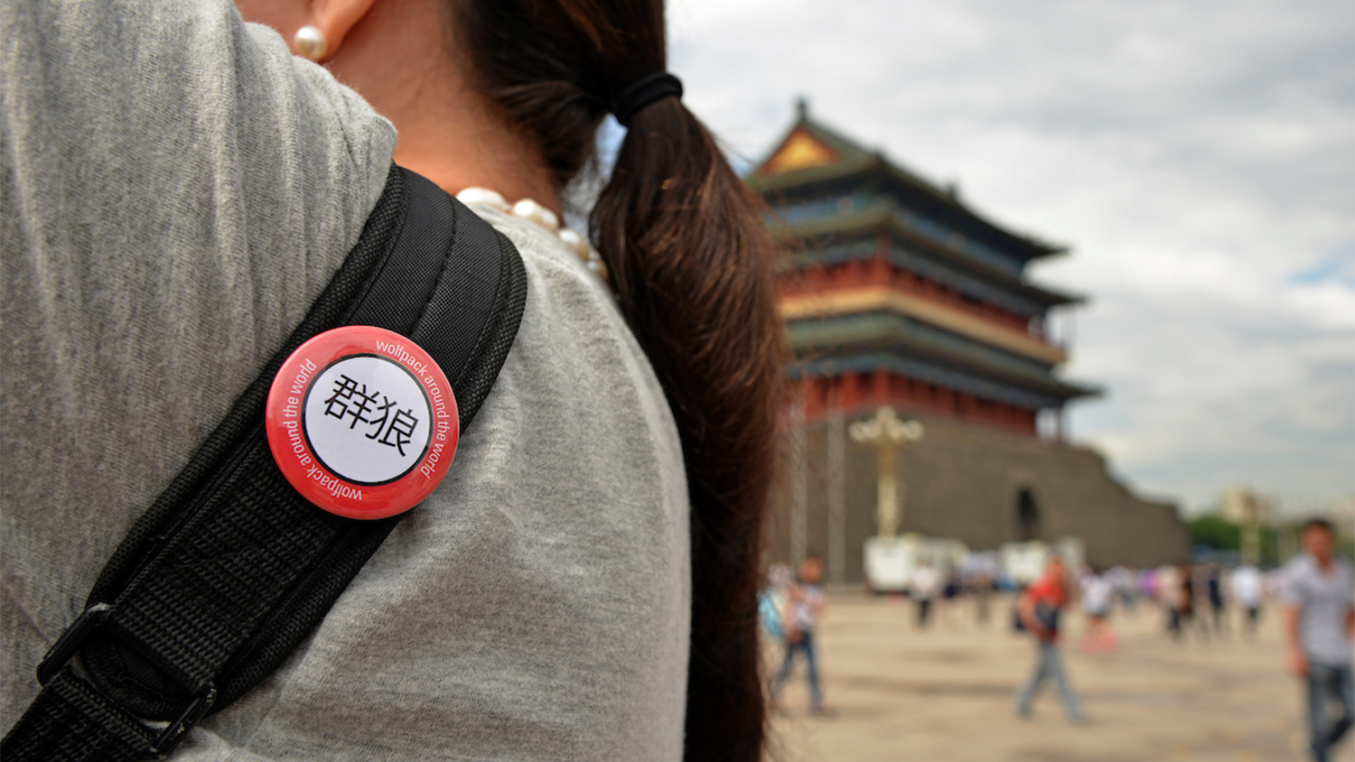 Close up of a study abroad button on a student's backpack, with a building in China in the background
