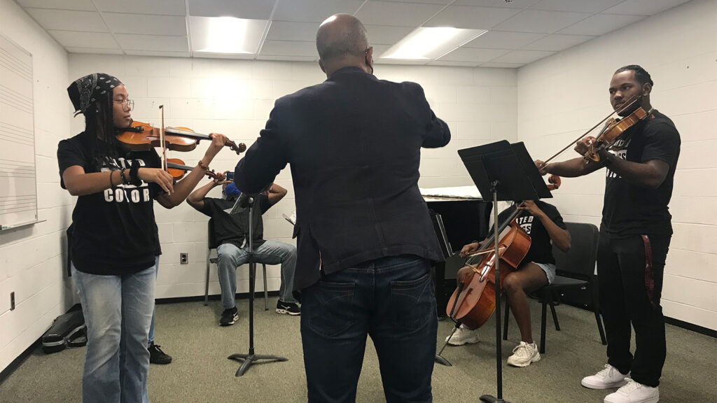 DBR and a small group of students play their string instruments in a circle