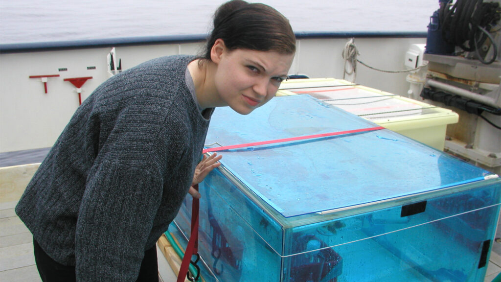 Janet Goins rests her hand on a large glass case filled with water on board a boat