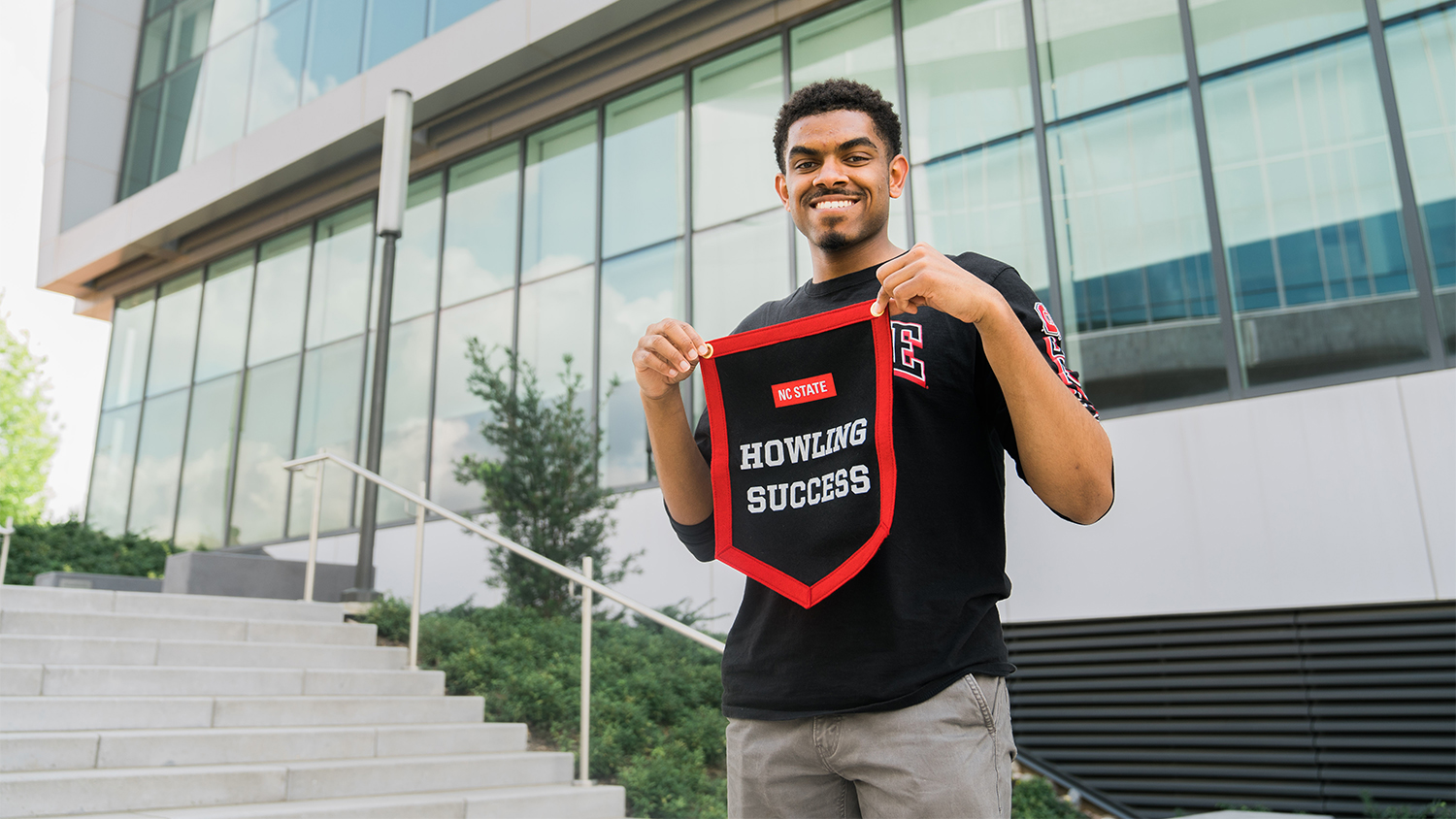 Joshua Wright holds a black, red and white pennant that reads "Howling Success" outside of Hunt Library