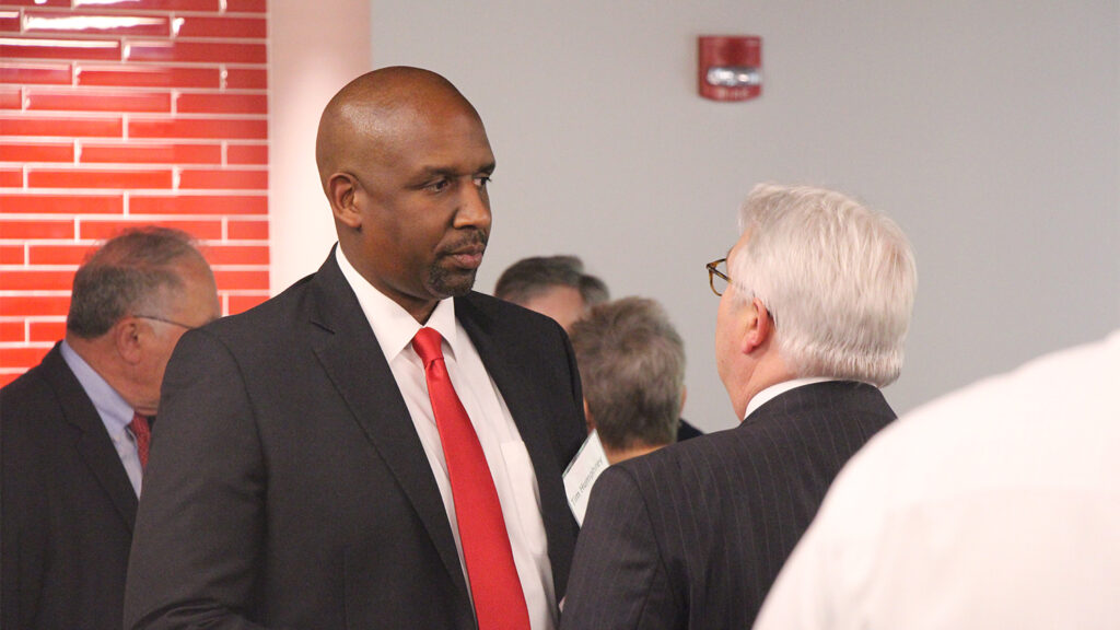 Humphrey talks with Chancellor Randy Woodson in front of a white wall with other people conversing behind them